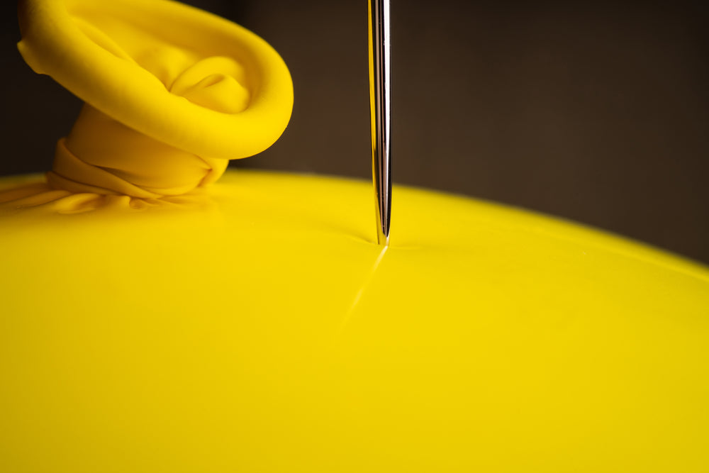 Feature image for this page, showcasing a needle being held against a yellow latex balloon.